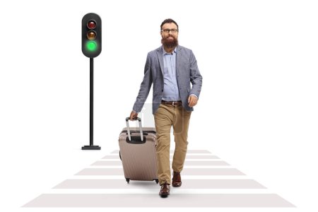 Téléchargez les photos : Portrait complet d'un homme barbu tirant une valise et traversant une rue à un passage pour piétons isolé sur fond blanc - en image libre de droit