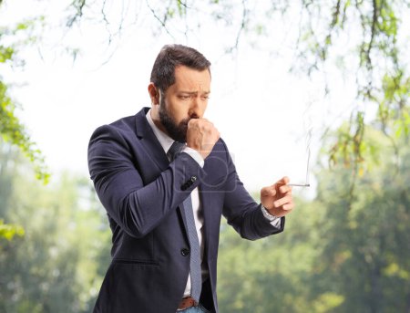 Téléchargez les photos : Homme fumant et toussant à l'extérieur dans un parc - en image libre de droit