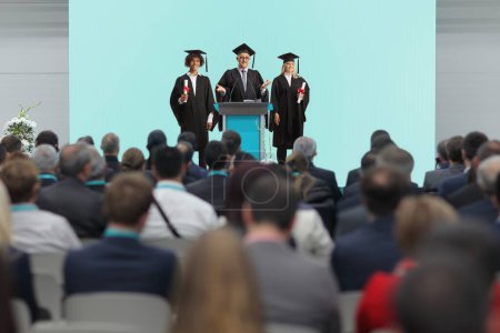 Photo for Students of honor and a dean standing on a podium in front of people in the audience - Royalty Free Image