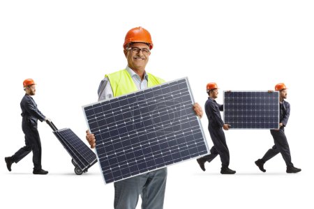 Foto de Sonriente ingeniero varón maduro sosteniendo un panel solar y los trabajadores caminando detrás aislados sobre fondo blanco - Imagen libre de derechos