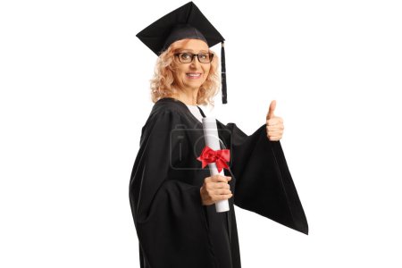 Photo for Mature woman in a graduation gown holding a diploma and showing thumbs up isolated on white background - Royalty Free Image