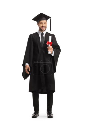 Photo for Full length portrait of a smiling man wearing a graduation gown and holding a diploma isolated on white background - Royalty Free Image