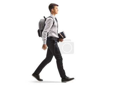 Estudiante masculino con una mochila en camisa y corbata sosteniendo libros y caminando aislado sobre fondo blanco