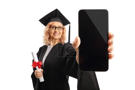 Photo for Cheerful woman in a black graduation gown holding a diploma and showing a smartphone isolated on white background - Royalty Free Image