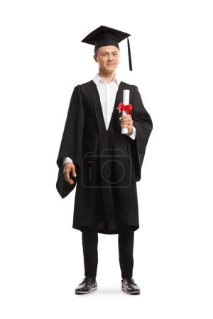Photo for Full length portrait of a smiling male student wearing a graduation gown and holding a diploma isolated on white background - Royalty Free Image