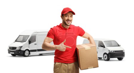 Photo for Delivery guy standing in front of transport vans and pointing to a box isolated on white background - Royalty Free Image