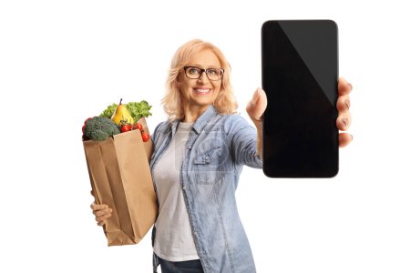 Téléchargez les photos : Femme mûre avec un sac d'épicerie tenant un smartphone isolé sur fond blanc - en image libre de droit