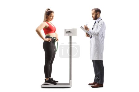 Téléchargez les photos : Médecin vérifiant le poids d'une jeune femme en tenue de sport isolée sur fond blanc - en image libre de droit