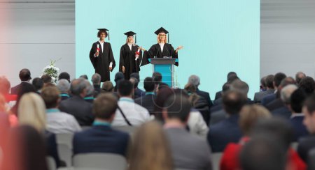 Photo for Graduate students of honor and a professor standing on a podium in front of people in the audience - Royalty Free Image