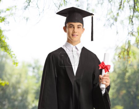 Photo for Smiling male graduate student in a park holding a diploma - Royalty Free Image