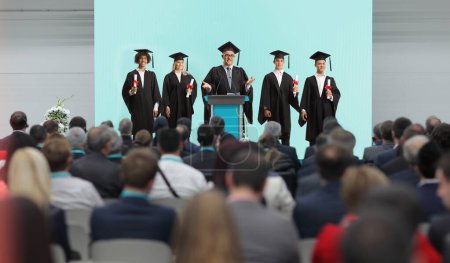Photo for Professor and graduate students standing on a podium in front of people in the audience - Royalty Free Image