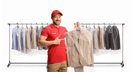 Téléchargez les photos : Porte-vêtements et travailleur de nettoyage à sec tenant un costume sur un cintre avec un couvercle en plastique isolé sur un dosseret blanc - en image libre de droit
