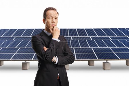 Téléchargez les photos : Homme d'affaires pensif tenant son menton devant des panneaux photovoltaïques isolés sur fond blanc - en image libre de droit