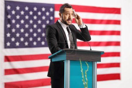 Foto de Empresario estresado preparándose para un discurso en un podio frente a la bandera de EE.UU. - Imagen libre de derechos