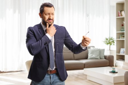 Foto de Joven dudoso sosteniendo un cigarrillo en una sala de estar en casa - Imagen libre de derechos