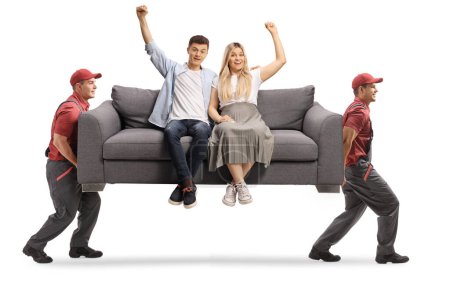 Téléchargez les photos : Déménageurs portant un jeune couple assis sur un canapé gris et gesticulant bonheur isolé sur fond blanc - en image libre de droit