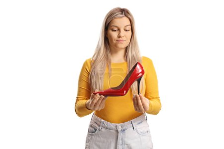 Foto de Joven hembra casual sosteniendo un zapato rojo de tacón alto y pensando aislado sobre fondo blanco - Imagen libre de derechos