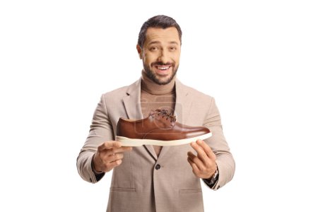 Téléchargez les photos : Jeune homme montrant une chaussure en cuir marron et souriant isolé sur fond blanc - en image libre de droit