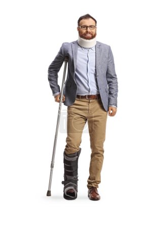 Foto de Retrato de cuerpo entero de un hombre con cuello y bota ortopédica de pie con una muleta aislada sobre fondo blanco - Imagen libre de derechos