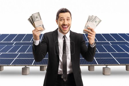 Photo for Excited man in a black suit holding stacks of money in front of a solar farm isolated on white background - Royalty Free Image