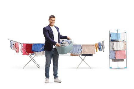 Foto de Retrato de cuerpo entero de un joven sosteniendo una cesta de lavandería frente a líneas de lavado aisladas sobre fondo blanco - Imagen libre de derechos