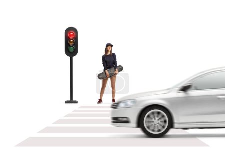 Photo for Full length portrait of a female skater holding a skateboard and waiting at traffic lights isolated on white background - Royalty Free Image