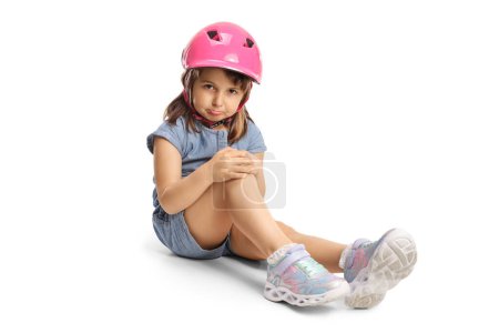 Photo for Sad little girl with a helmet sitting on the ground and holding her knee isolated on white background - Royalty Free Image