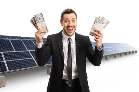 Photo for Businessman holding stacks of cash in both hands in front of solar panels isolated on white background - Royalty Free Image