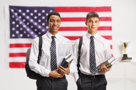 Téléchargez les photos : Étudiants blancs et afro-américains en chemise et cravate tenant des livres et debout devant un drapeau américain - en image libre de droit