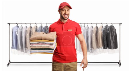 Foto de Trabajador masculino sosteniendo una pila de ropa doblada frente a bastidores de ropa en tintorerías aisladas sobre un fondo blanco - Imagen libre de derechos