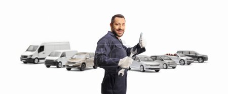 Photo for Auto mechanic holding a wrench in front of parked vehicles and gesturing thumbs up isolated on white background - Royalty Free Image