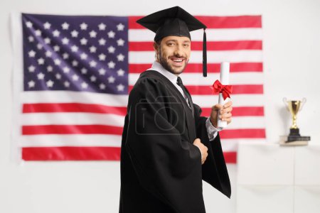 Photo for Graduate male student holding a diploma and smiling with the USA flag in the background - Royalty Free Image