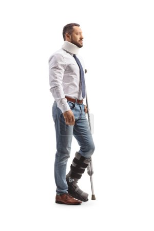 Foto de Perfil de un joven con bota ortopédica y cuello cervical de pie con una muleta aislada sobre fondo blanco - Imagen libre de derechos