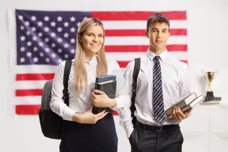 Photo for Male and female student holding books and standing in front of a USA fla - Royalty Free Image