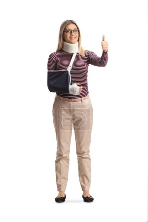 Photo for Full length portrait of a young injured woman with arm sling and cervical collar gesturing thumbs up isolated on white background - Royalty Free Image