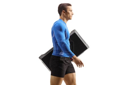 Photo for Profile shot of a fit man walking and carrying an aerobic stepper isolataed on white background - Royalty Free Image
