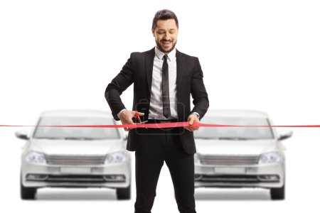 Foto de Empresario cortando una cinta roja delante de una fila de coches plateados aislados sobre fondo blanco - Imagen libre de derechos