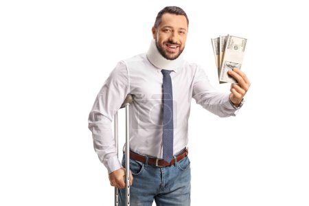 Téléchargez les photos : Homme blessé avec un collier cervical appuyé sur des béquilles et tenant des piles d'argent isolées sur fond blanc - en image libre de droit