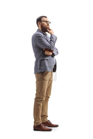 Foto de Plano de longitud completa de un hombre barbudo pensando y sosteniendo su barbilla aislada sobre fondo blanco - Imagen libre de derechos