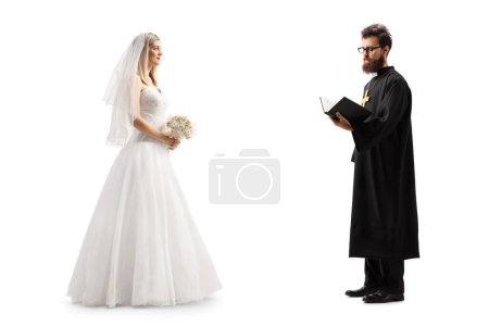 Photo for Full length profile shot of a bride standing with a priest holding a bible isolated on white background - Royalty Free Image