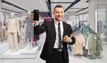 Téléchargez les photos : Homme d'affaires montrant un téléphone portable à l'intérieur d'un magasin de vêtements - en image libre de droit
