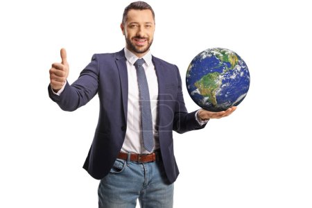 Téléchargez les photos : Jeune homme tenant la planète terre sur sa main et geste pouces vers le haut isolé sur fond blanc - en image libre de droit