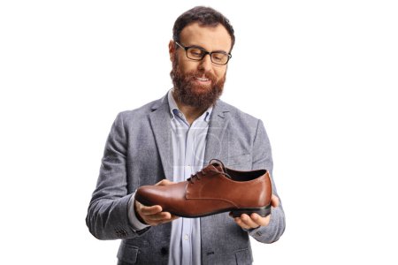 Téléchargez les photos : Jeune homme barbu tenant une élégante chaussure en cuir marron et souriant isolé sur fond blanc - en image libre de droit