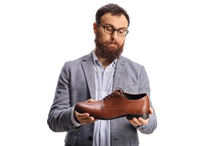 Téléchargez les photos : Homme barbu confus tenant une chaussure en cuir brun isolé sur fond blanc - en image libre de droit