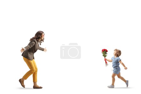 Téléchargez les photos : Petite fille tenant des roses rouges et courant vers une jeune femme isolée sur fond blanc - en image libre de droit