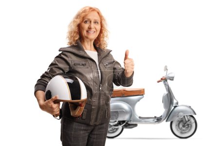 Photo for Mature woman with a scooter holding a helmet and gesturing thumbs up isolated on white background - Royalty Free Image