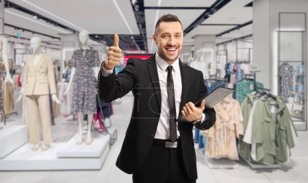 Foto de Empresario con un portapapeles y documentos que muestran pulgares hacia arriba dentro de una tienda de ropa - Imagen libre de derechos