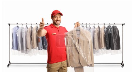 Photo for Dry cleaning worker holding a suit on a hanger with a plastic cover and gesturing thumbs up isolated on a white backgroun - Royalty Free Image