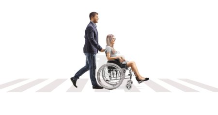 Photo for Full length profile shot of a young man pushing a young woman in a wheelchair across street isolated on white background - Royalty Free Image
