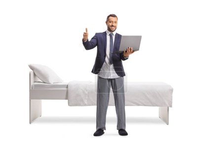 Téléchargez les photos : Homme d'affaires en costume et pyjama bas tenant un ordinateur portable et geste pouces vers le haut isolé sur fond blanc - en image libre de droit